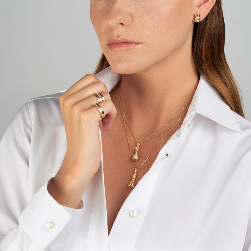 Woman wearing a white shirt with gold jewelry against a gray background
