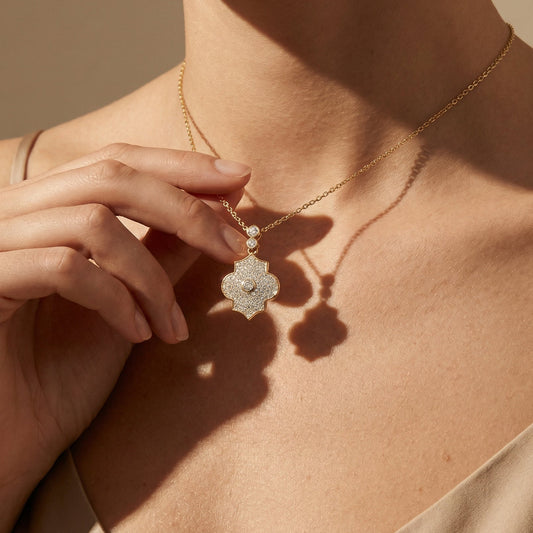 Close-up of a person wearing a gold and diamond necklace with a decorative pendant against a neutral background