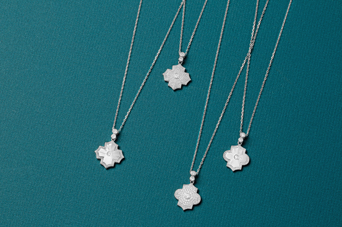 Three silver necklaces with floral pendants on a teal background