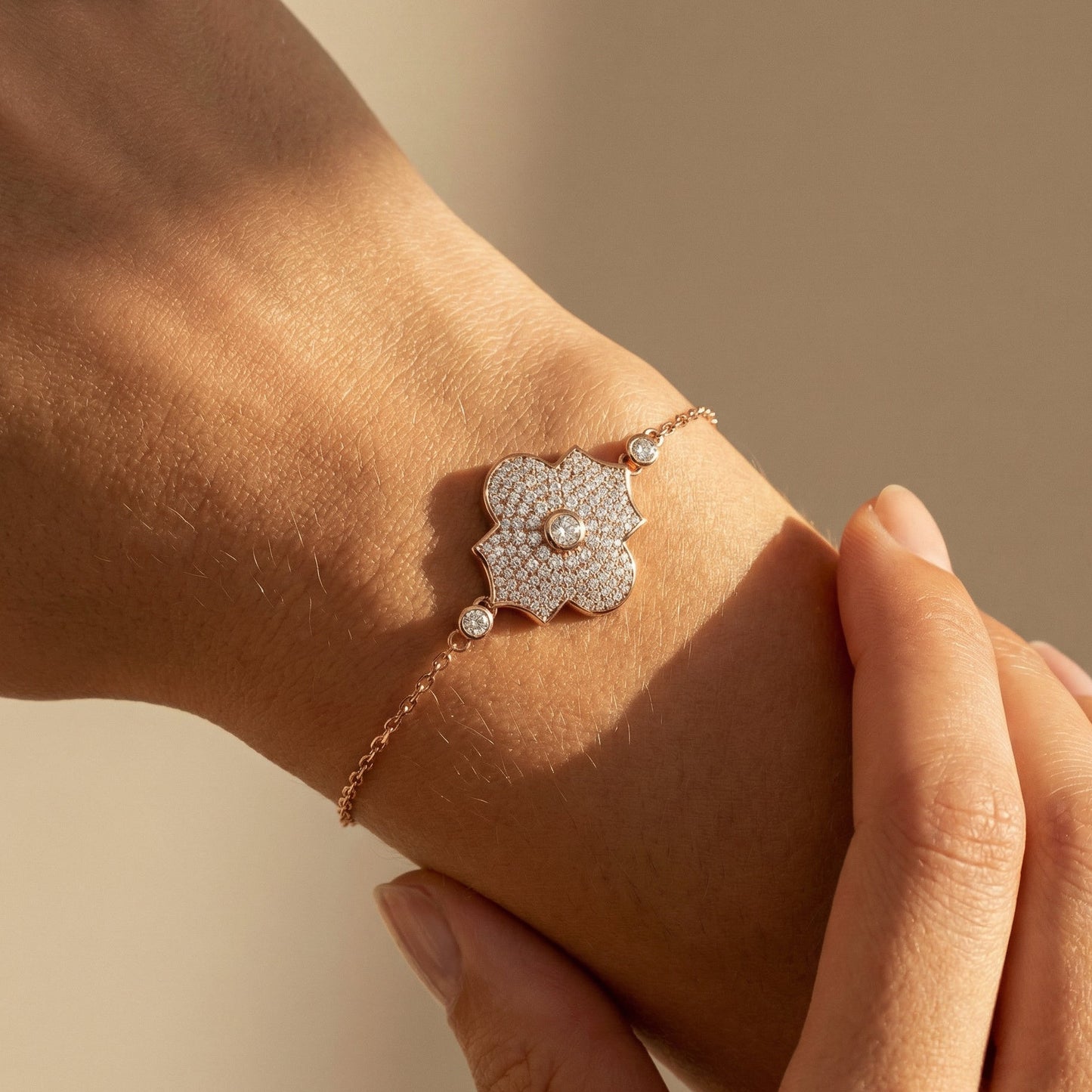 Rose gold white diamond pave chain bracelet with a flower motif worn by a model on a neutral background 