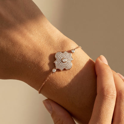 Rose gold white diamond pave chain bracelet with a flower motif worn by a model on a neutral background 