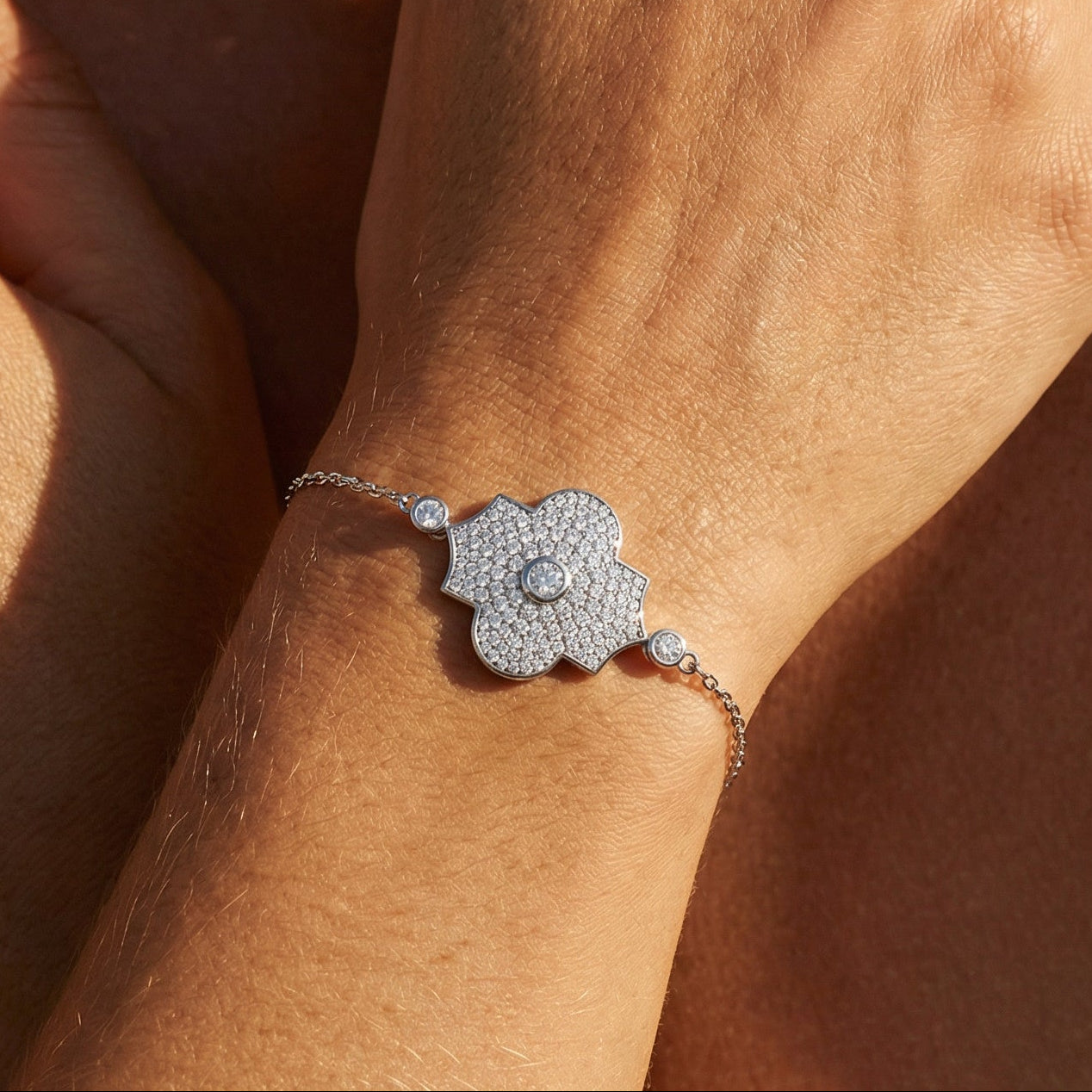 white gold white diamond pave chain bracelet with a flower motif worn on a models hand and neutral background 