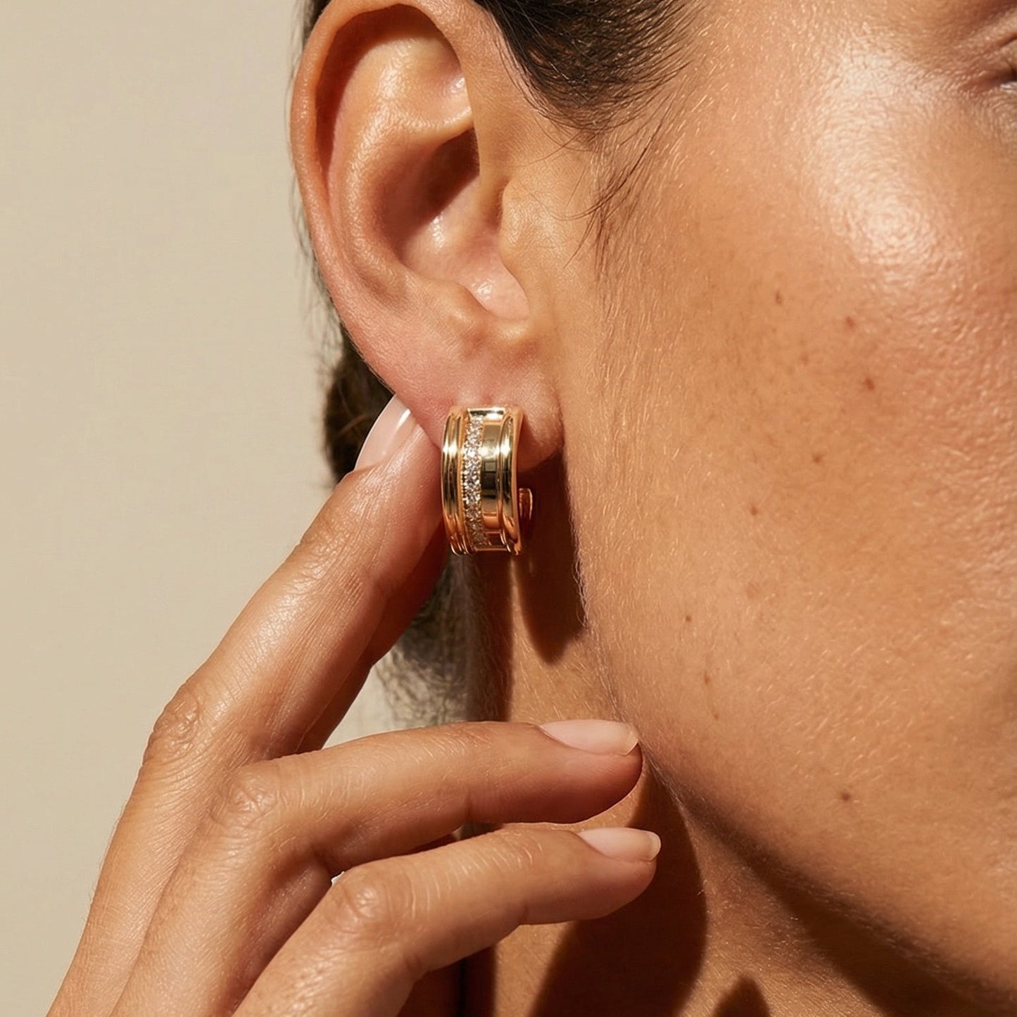 Close-up of a person wearing gold hoop earrings with a neutral background