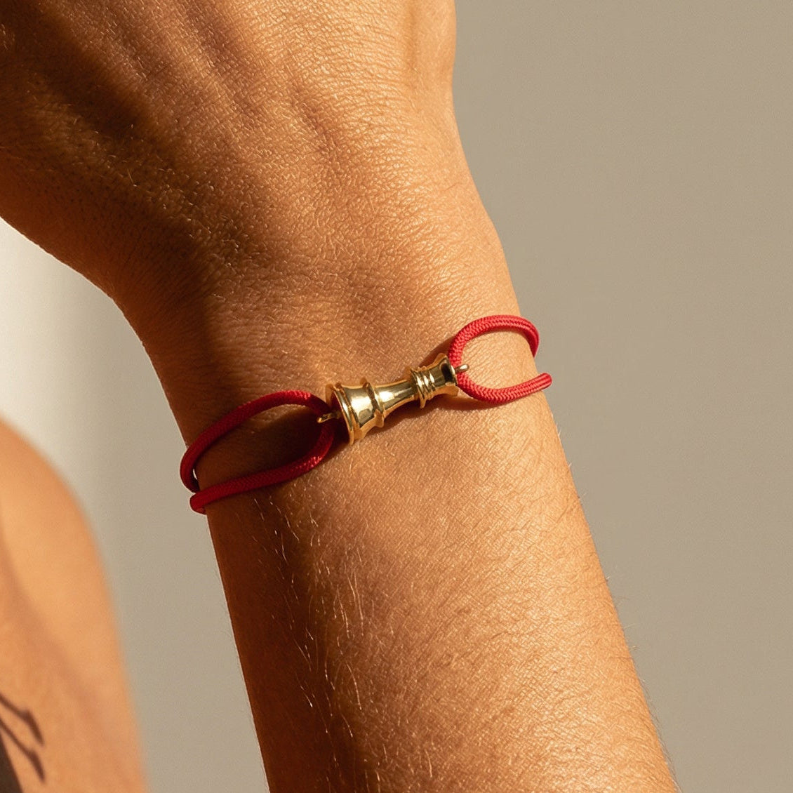Close-up of a person wearing a red bracelet with a gold chess queen clasp on a neutral background