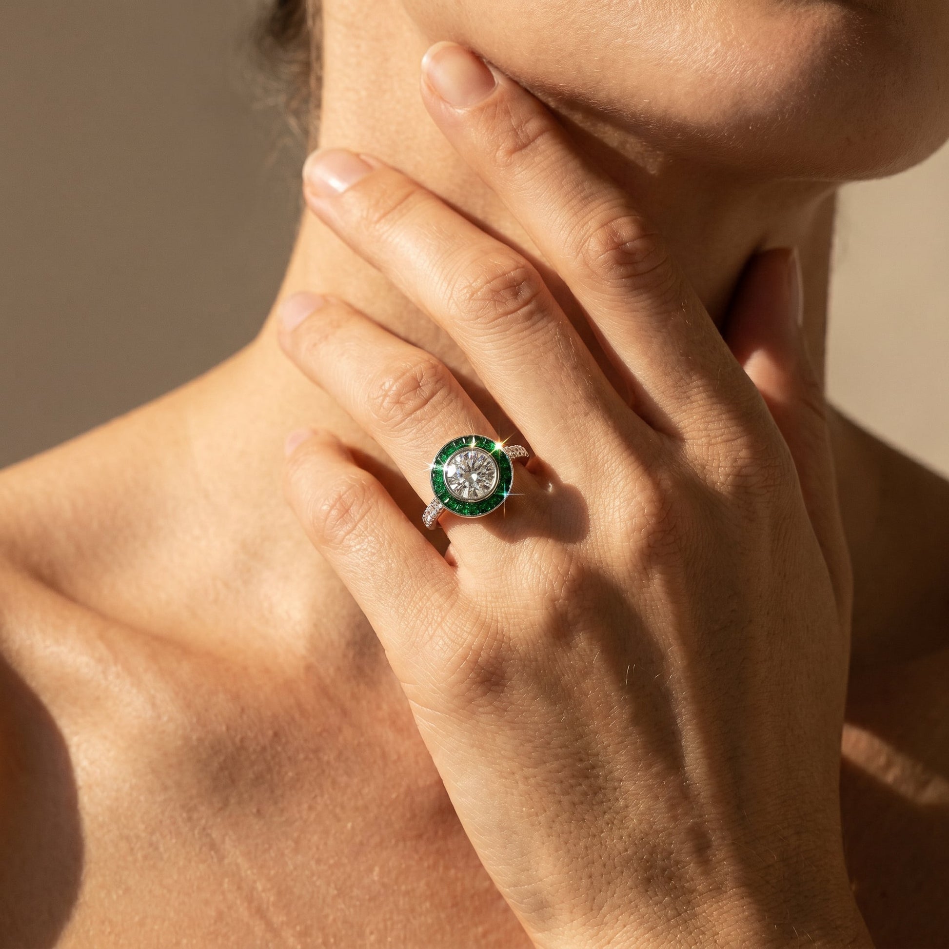 Platinum art deco style engagement ring with white diamond round brilliant and emerald halo on a models hand and a neutral background 