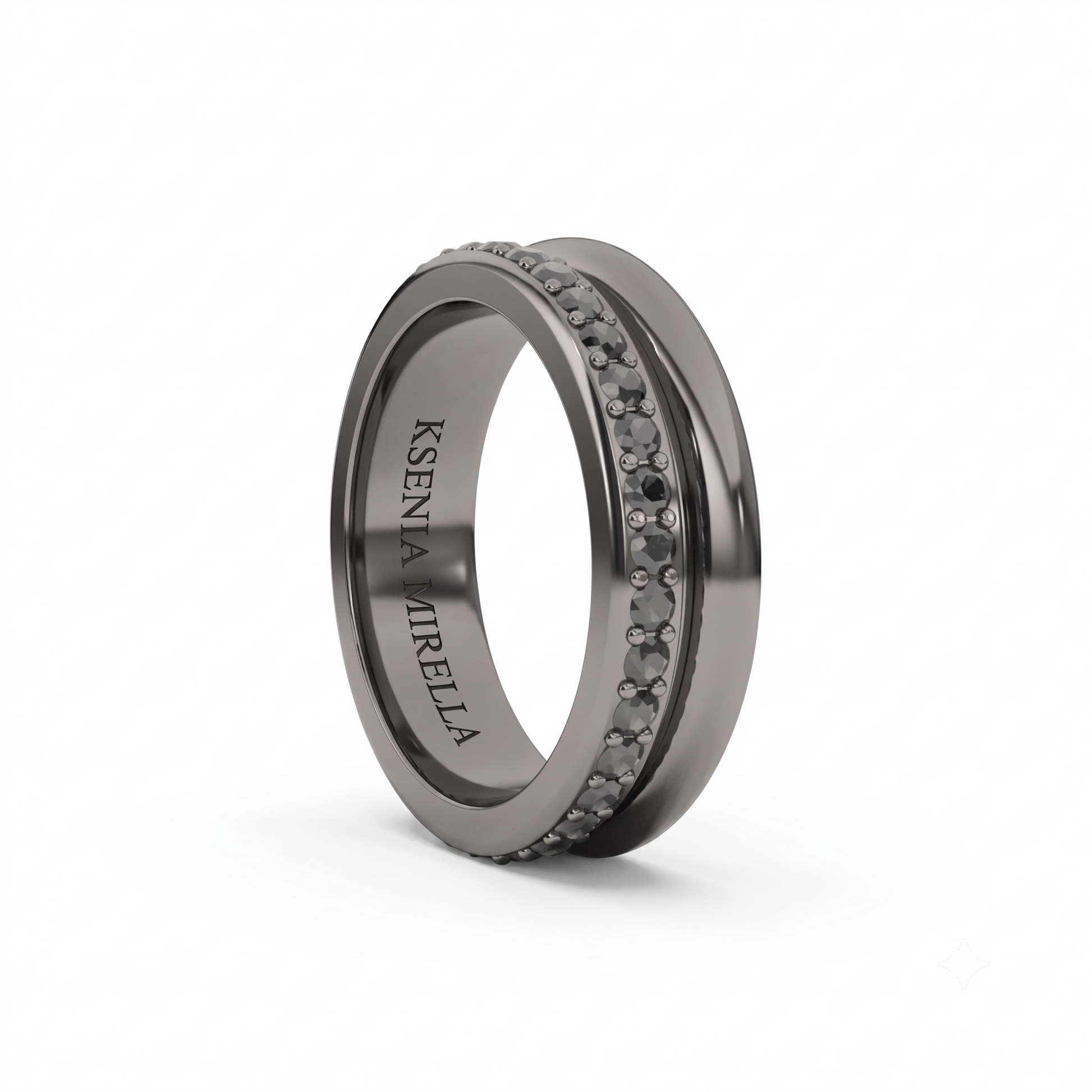 A dark gray metallic ring with a double row of small round clear stones on the front, featuring the engraved name 'Ksenia Mirella' on the inner band, shown on a white background.