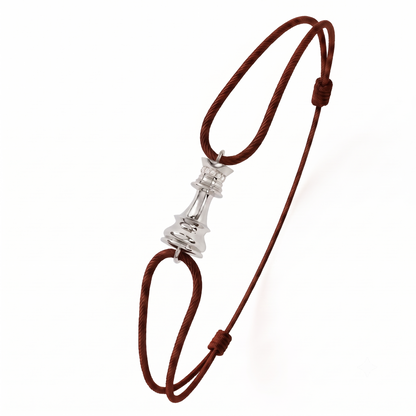 A brown braided cord bracelet with a polished white gold white diamond chess piece charm in the center, displayed on a clean white background.