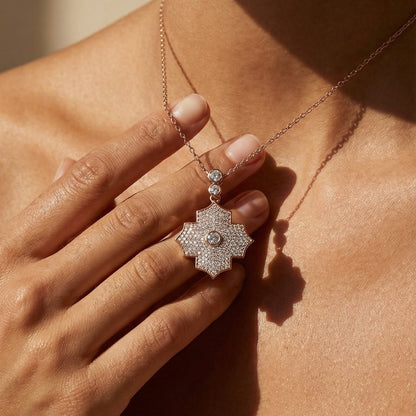 Close-up of a hand wearing a diamond necklace with a floral pendant.