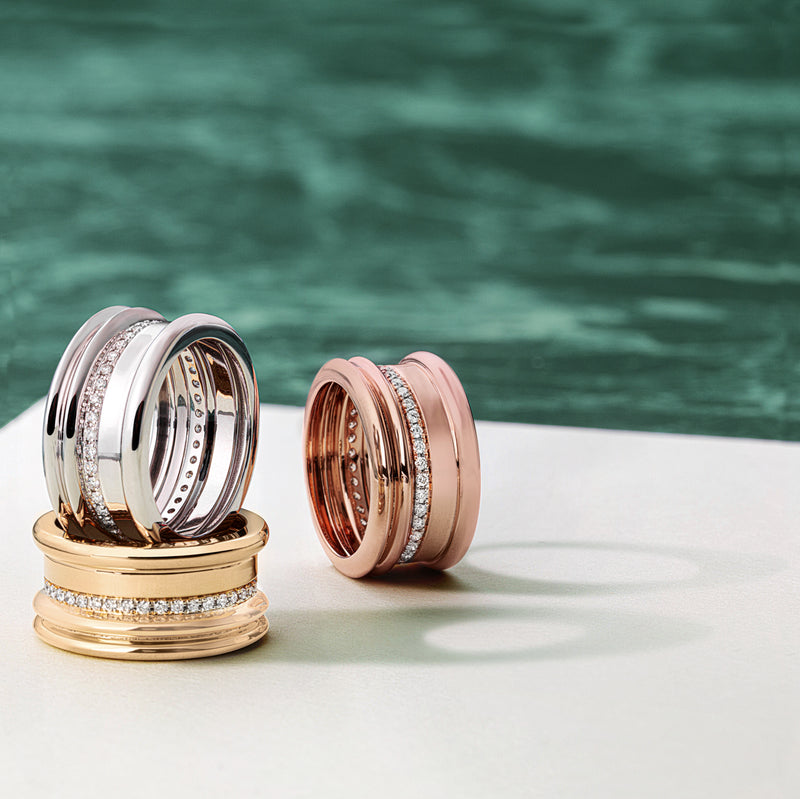 Three rings in gold, silver, and rose gold on a white surface with a green blurred background