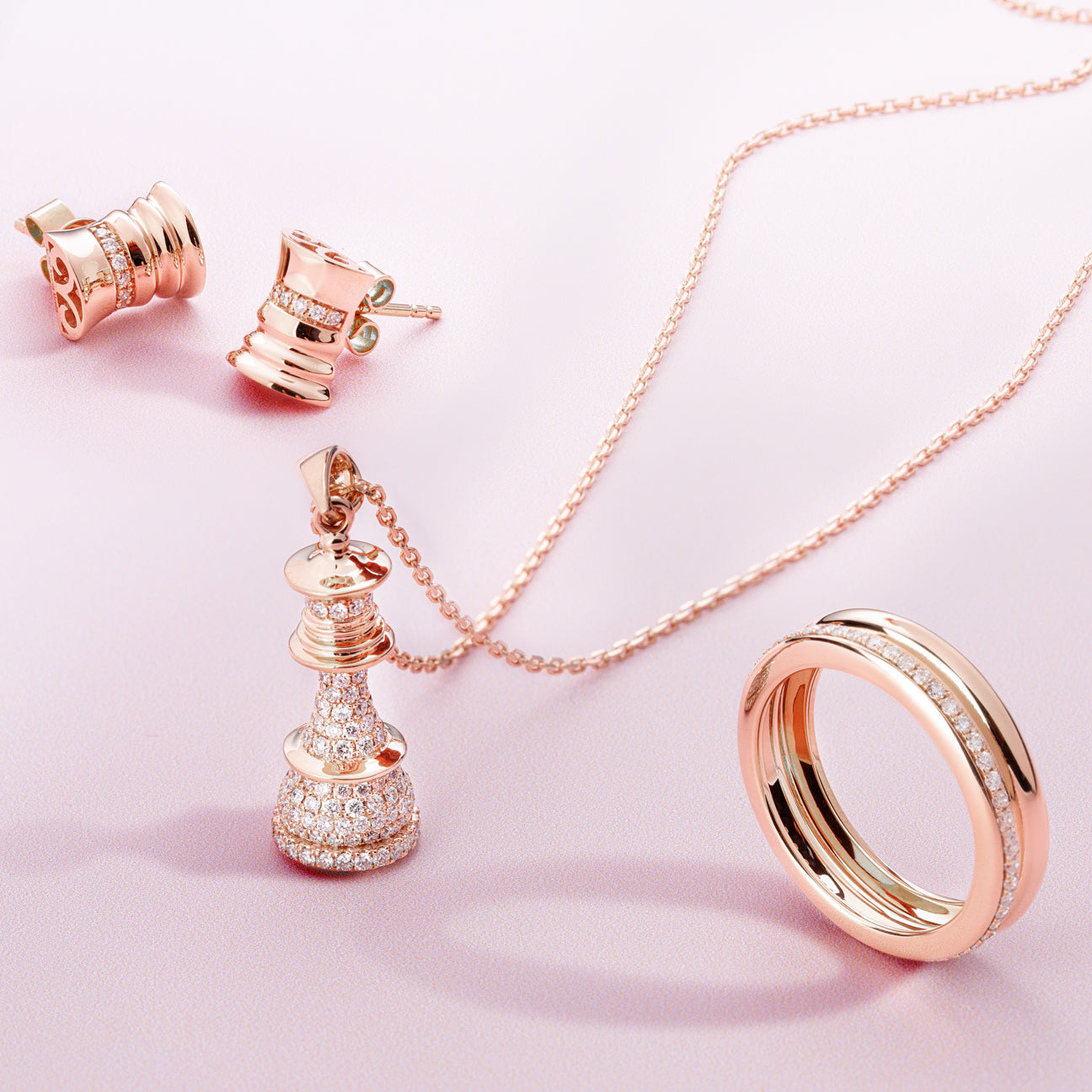 Rose gold jewelry set including earrings, necklace, and ring on a pink background