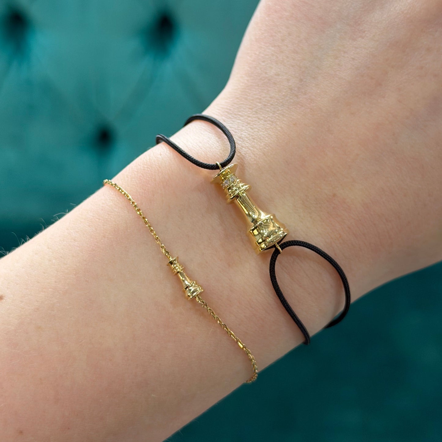 Close-up of a wrist wearing two gold bracelets on a blurred teal background