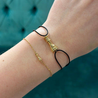 Close-up of a wrist wearing two gold bracelets on a blurred teal background Ksenia Mirella Jewellery Queen Icon Chain Bracelet