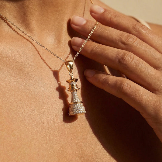 Close-up of a person wearing a gold chess Queen necklace with a pendant against a beige background