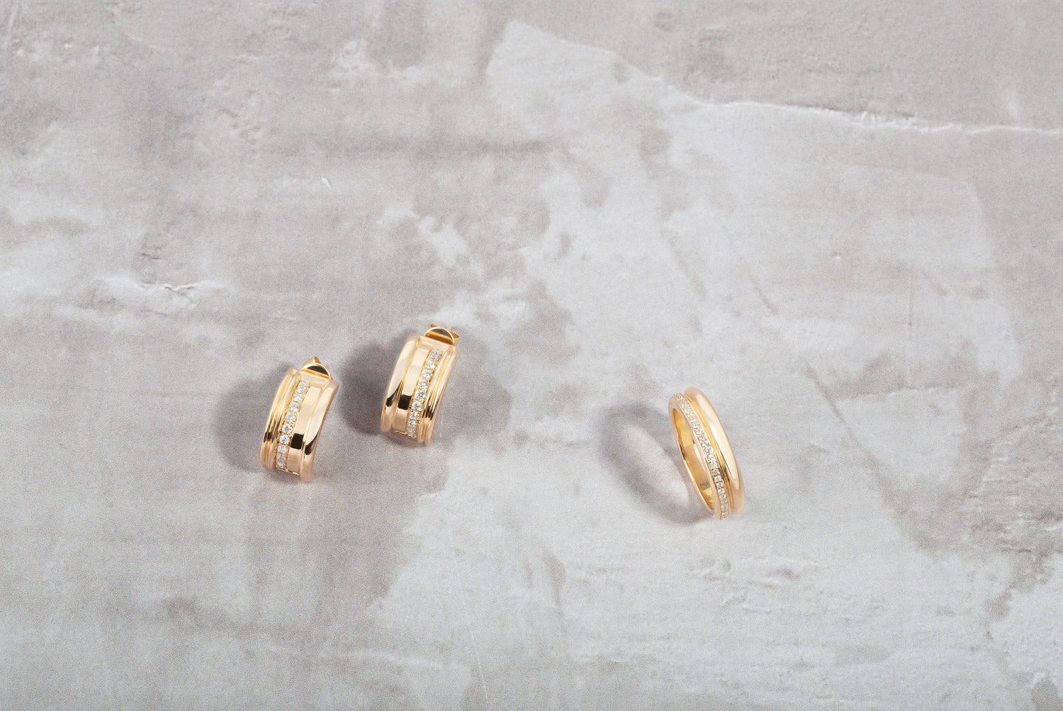 Two gold hoop earrings on a light gray marble surface
