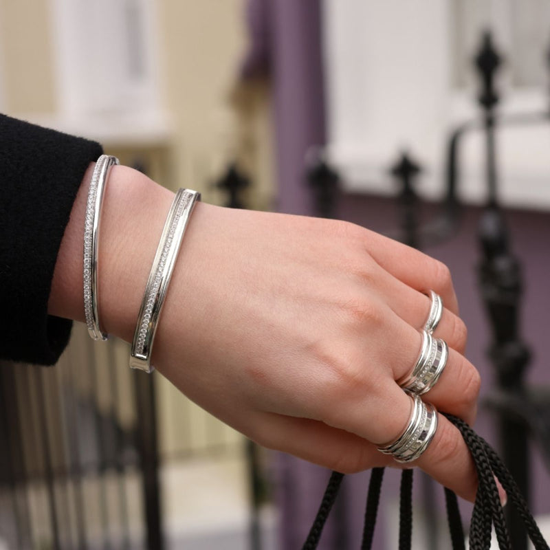 Hand wearing white gold diamond bangles and stacked silver rings, holding black bag straps