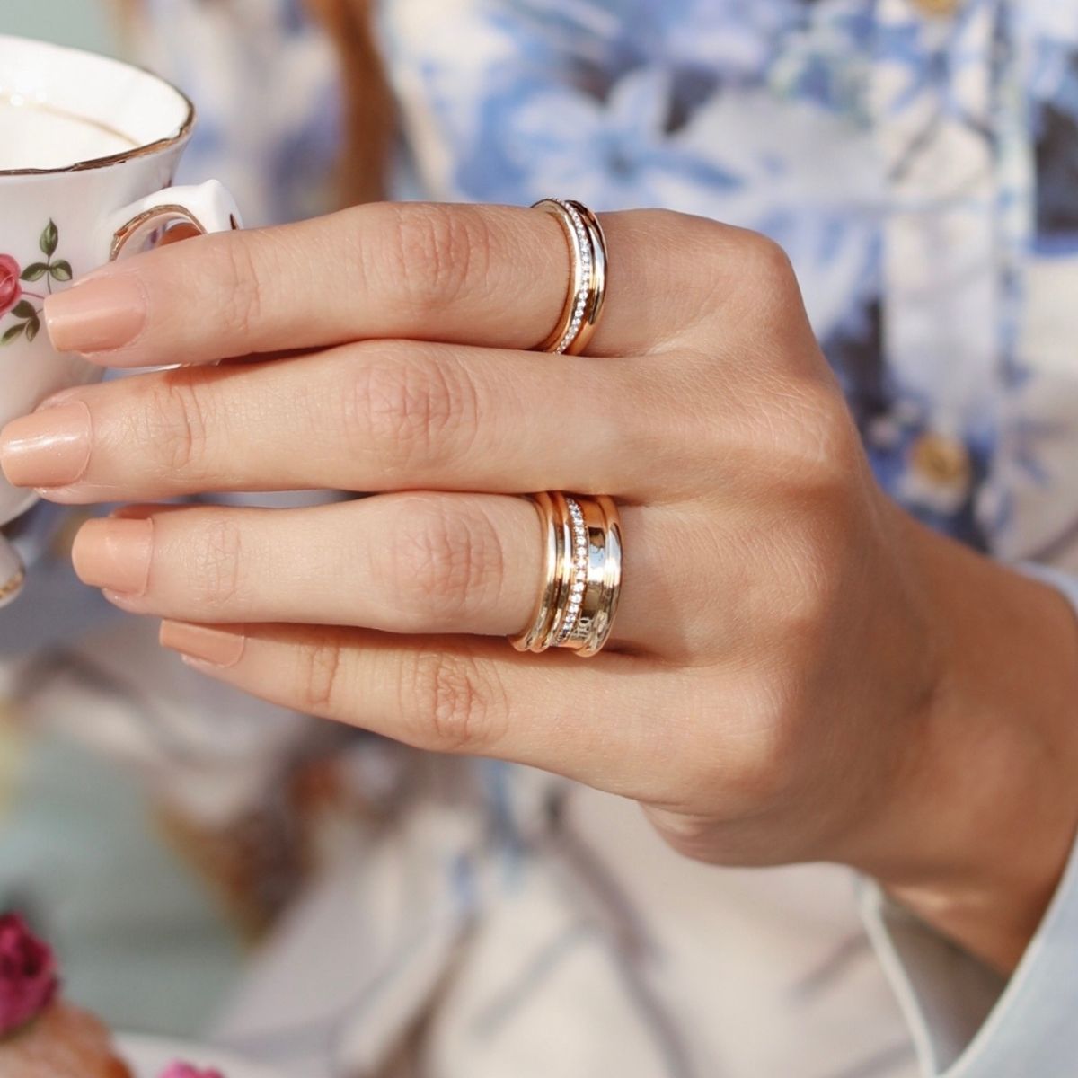 Stacked yellow and white gold diamond rings by Ksenia Mirella Jewellery worn while holding a teacup