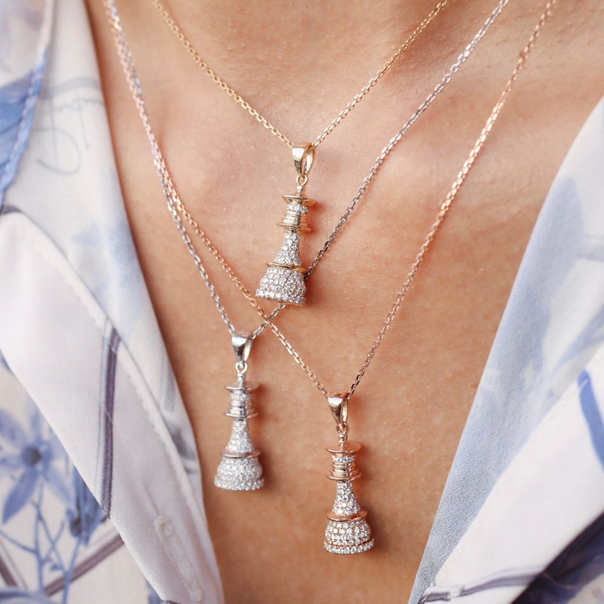 A person wearing multiple necklaces with yellow gold settings and white diamond pendants.