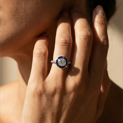 Close-up of a hand wearing a art deco white diamond and blue sapphire ring with a blue gemstone, touching the face. Ksenia Mirella Jewellery