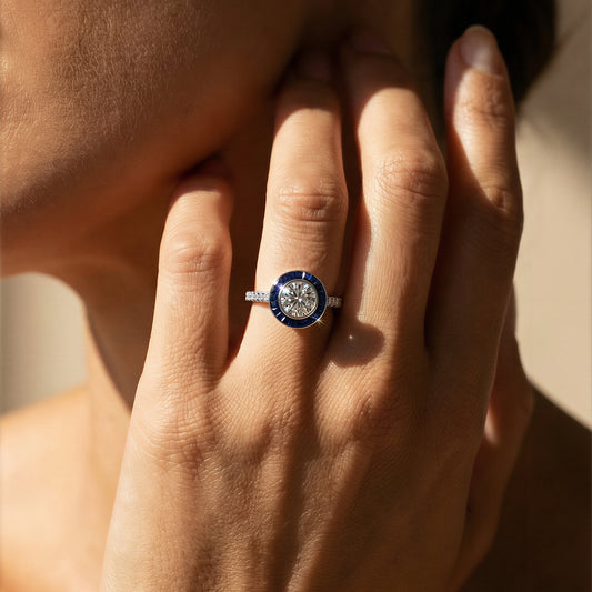 Close-up of a hand wearing a art deco white diamond and blue sapphire ring with a blue gemstone, touching the face. Ksenia Mirella Jewellery