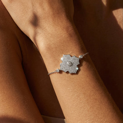 Silver bracelet with a geometric design on a wrist against a brown background
