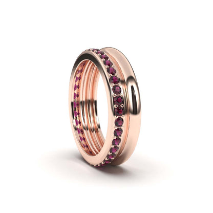 A rose gold ruby eternity ring with a series of graduated ruby weights set within its band, surrounded by a polished metallic rim.