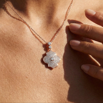 Necklace with a floral pendant worn by a person, with a hand touching the skin.