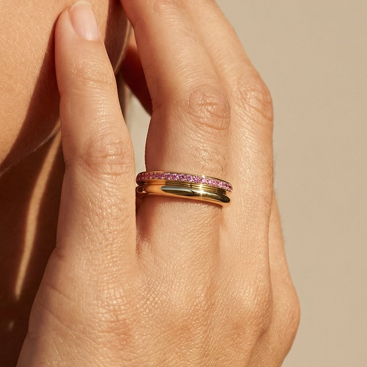 Close-up of a hand wearing a ring with a pink gemstone against a beige background