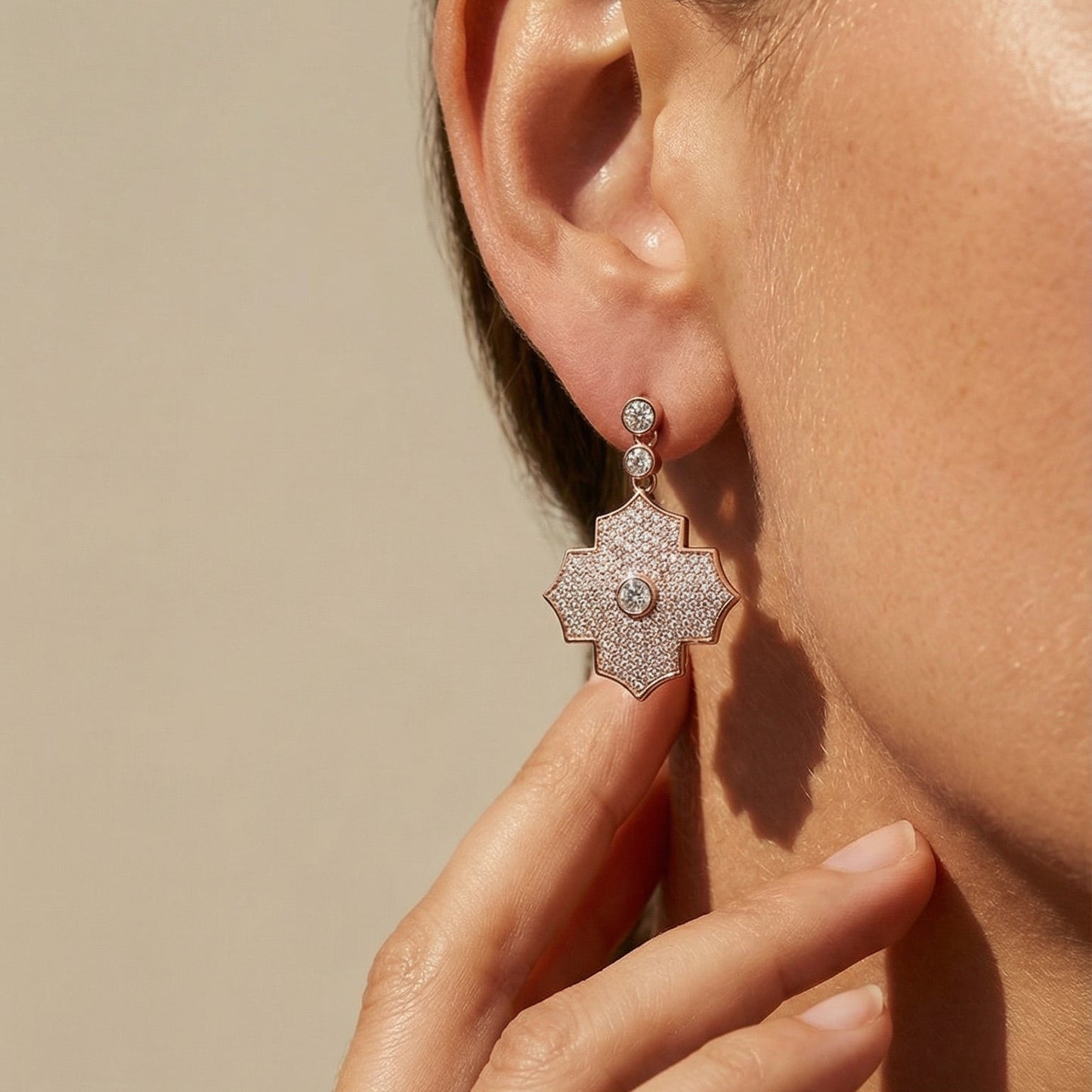 Close-up of a person wearing a rose gold earring with a beige background