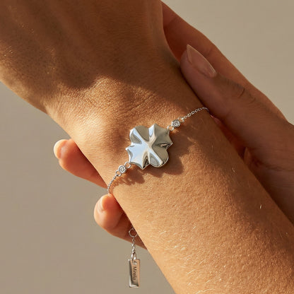 white gold bracelet with a clover-shaped charm on a wrist against a neutral background