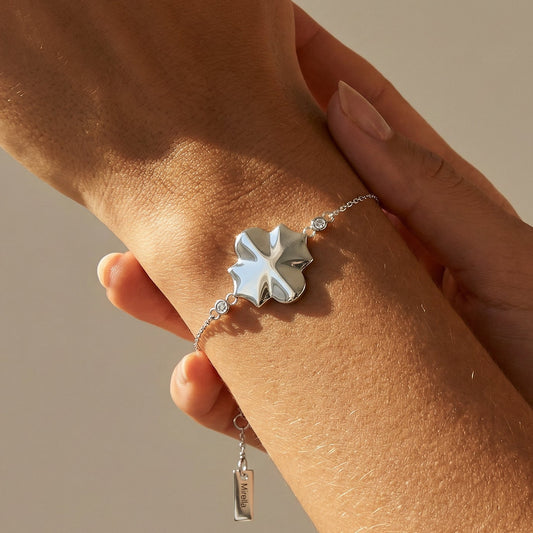 white gold bracelet with a clover-shaped charm on a wrist against a neutral background