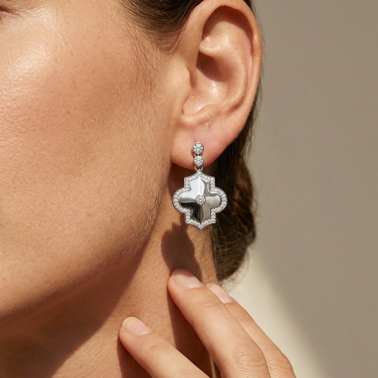 Close-up of a person wearing a white gold white diamond drop earring with a blurred background