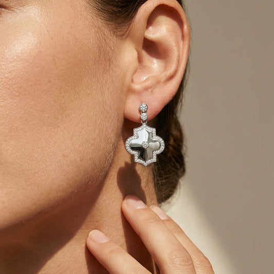 Close-up of a person wearing a white gold white diamond drop earring with a blurred background