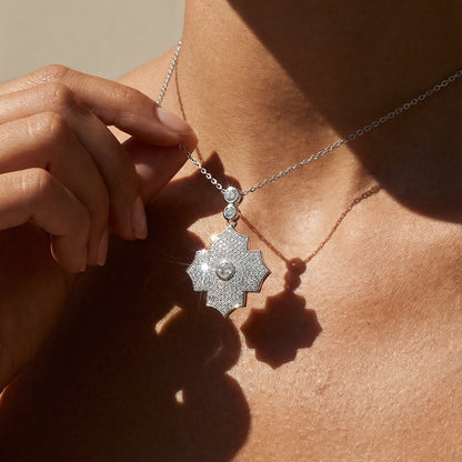 Close-up of a person wearing a white gold necklace with a pendant on a neutral background