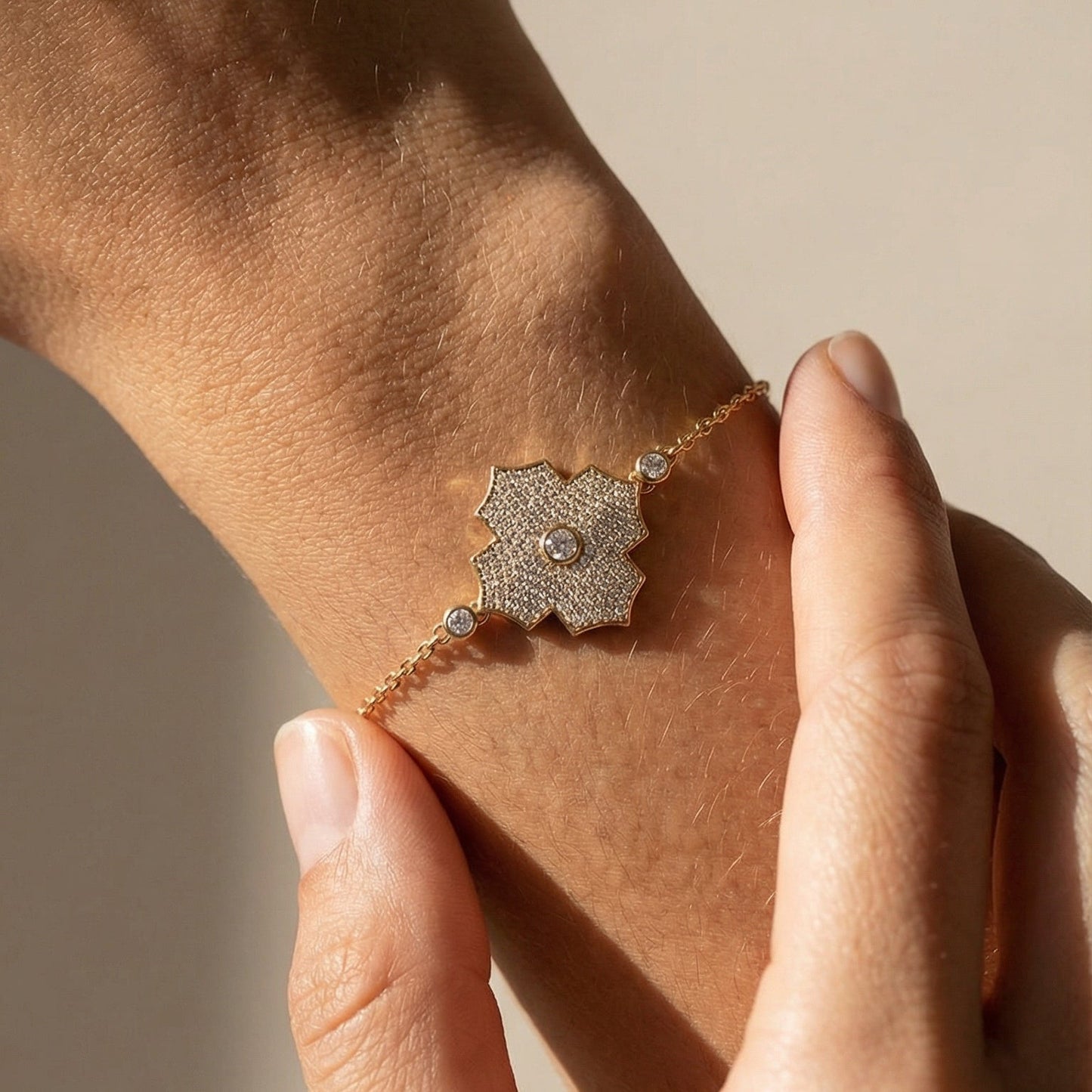 Close-up of a hand wearing a delicate bracelet with a textured clasp on a neutral background