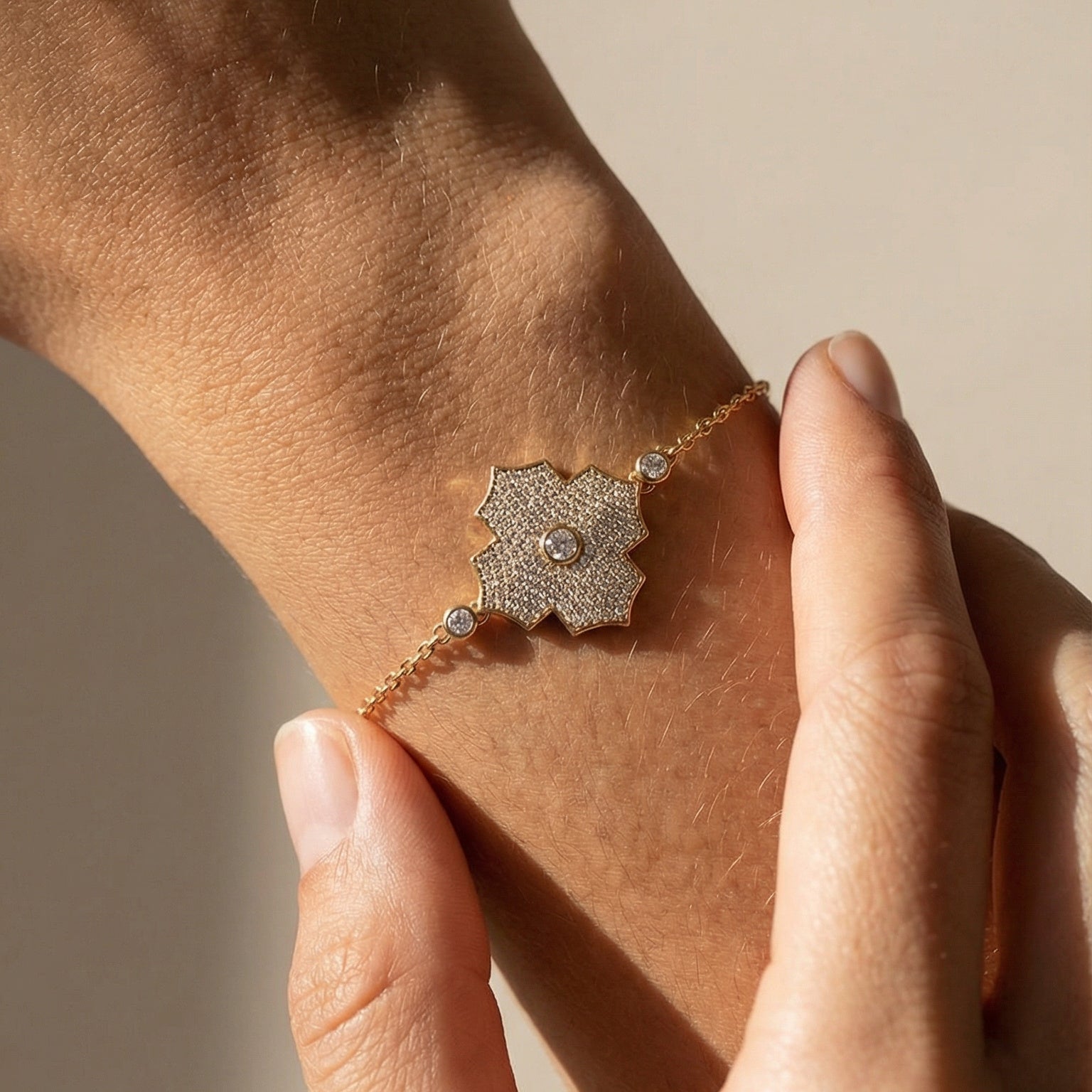 Close-up of a hand wearing a delicate bracelet with a textured clasp on a neutral background