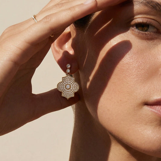 Close-up of a woman wearing a drop yellow gold full diamond pave earring with a neutral background