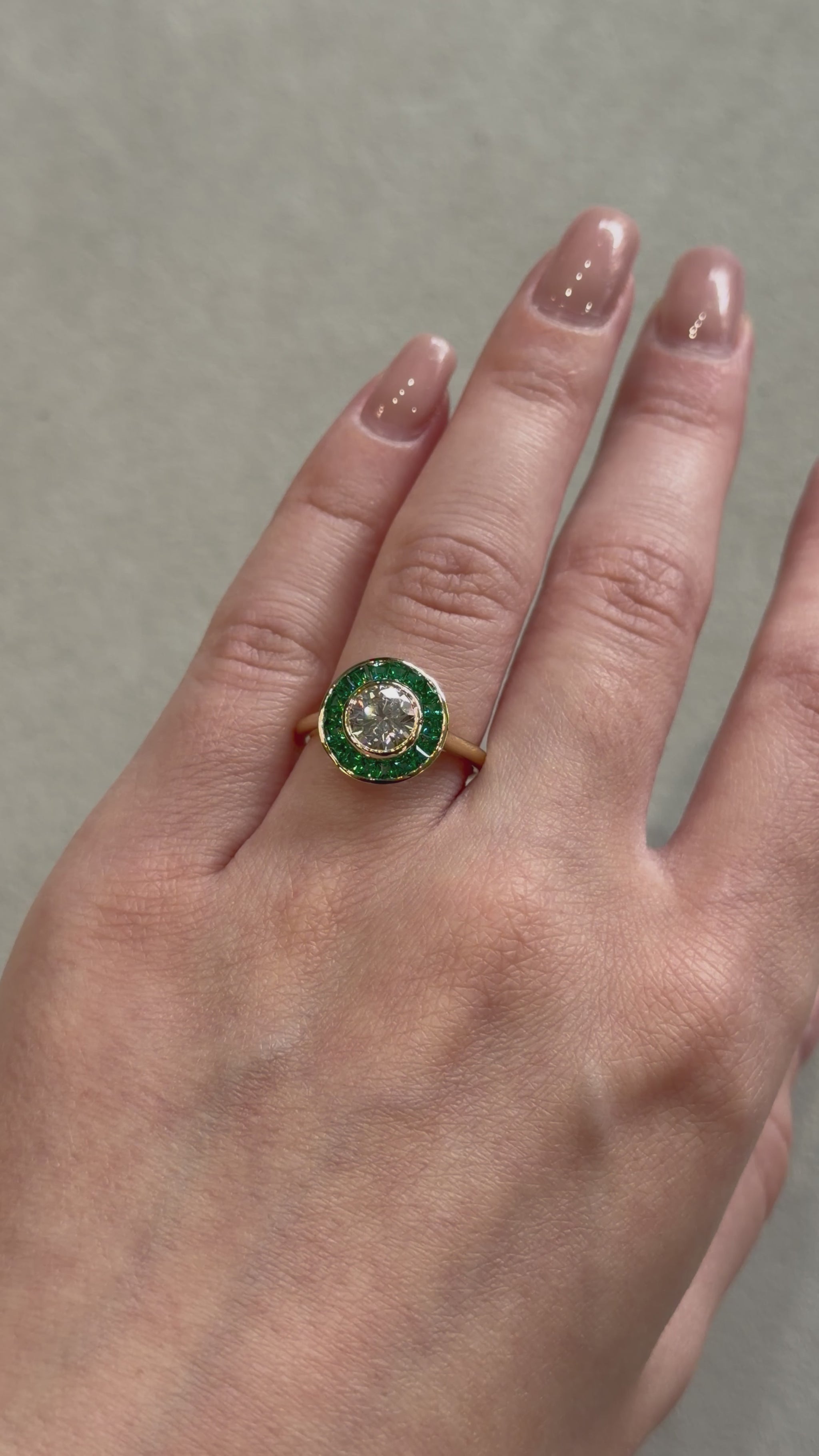 Art Deco style engagement ring on a yellow gold band with a green emerald halo and a white diamond in the center on a female hand 