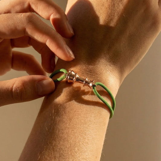 Person adjusting a green bracelet on their wrist against a neutral background